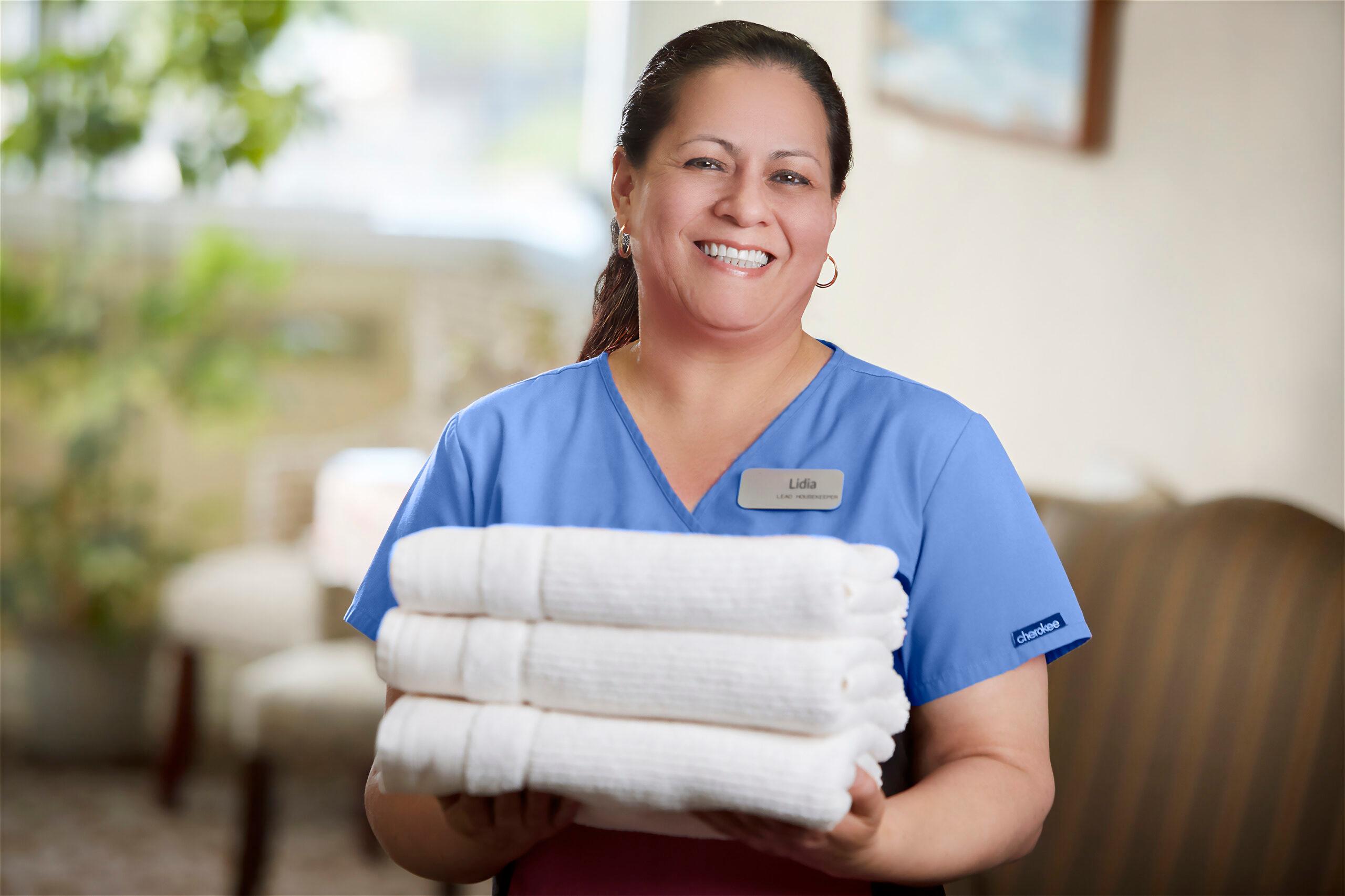 A smiling residential living employee holds a stack of towels.
