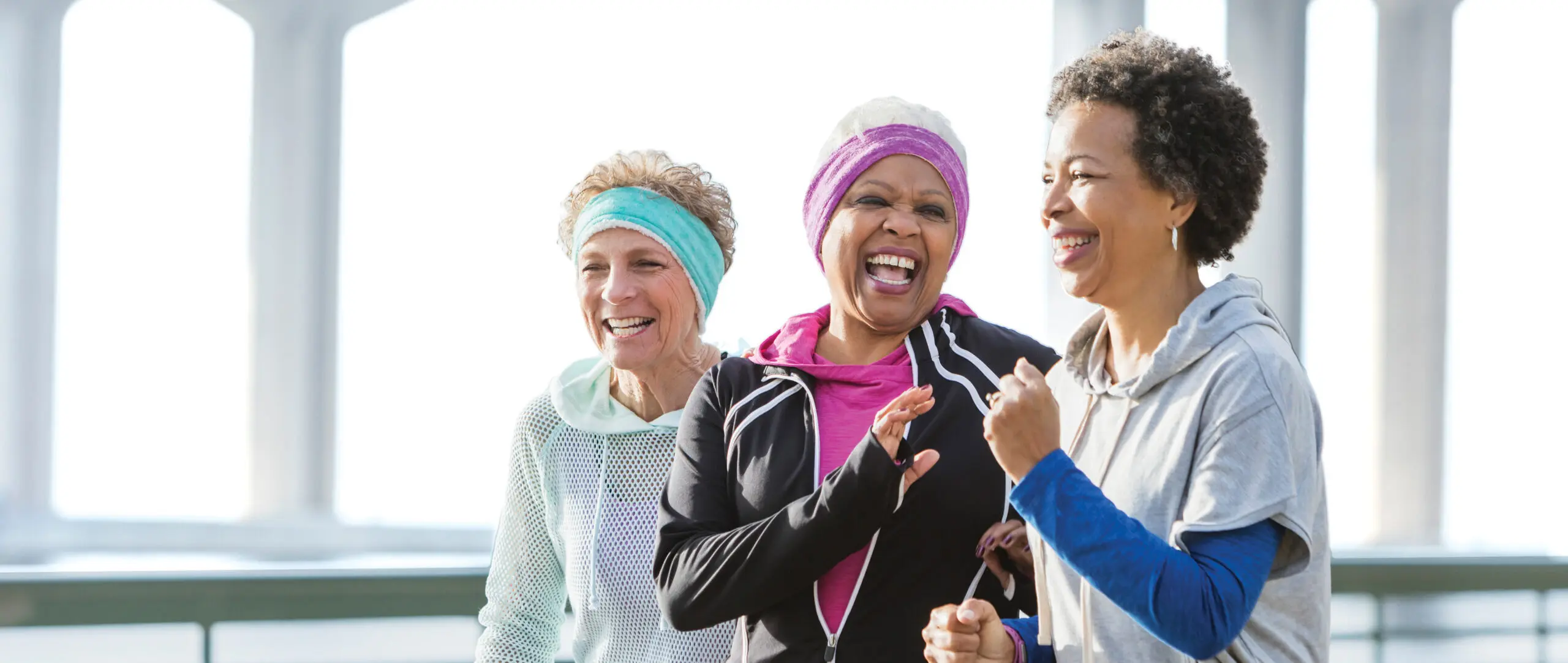 Three women talk and laugh as they power walk together on the waterfront.
